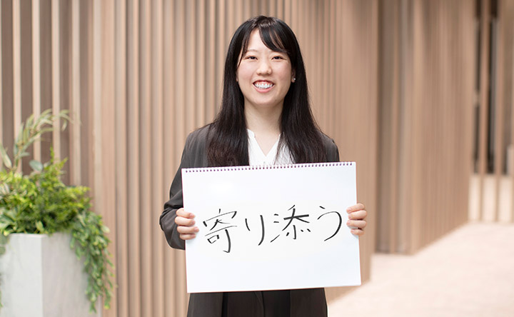 「寄り添う」という言葉を書いたスケッチブックを掲げる、笑顔の新沼